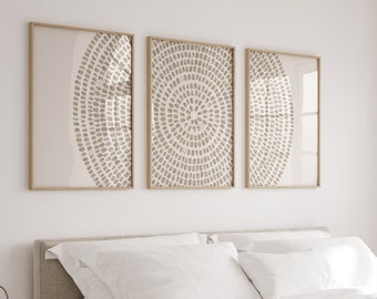 May include: A white bed with a beige knitted throw blanket and white pillows. Three framed prints with beige abstract designs hang on the wall above the bed.