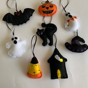 May include: A set of felt Halloween ornaments, including a black bat, a black cat, a pumpkin, a witch's hat, a ghost, a candy corn, and a black house with a ghost inside.