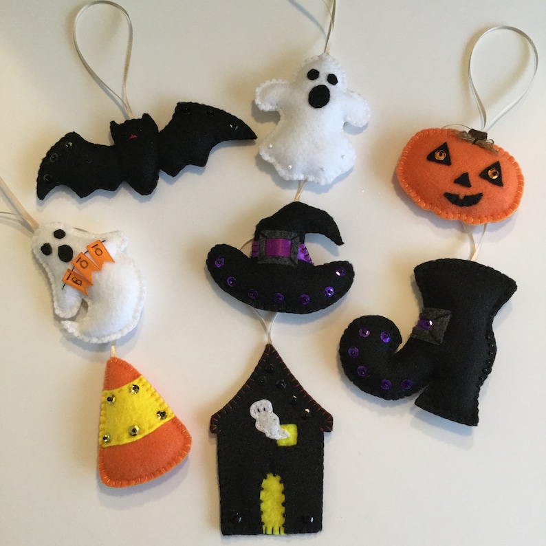 May include: A Halloween garland with felt ornaments. The ornaments include a bat, a ghost, a witch's hat, a pumpkin, a boot, a candy corn, and a house with a ghost inside.