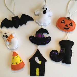 May include: A Halloween garland with felt ornaments. The ornaments include a black bat, a white ghost, a black witch's hat, a black boot, an orange pumpkin, a yellow and orange candy corn, and a black house with a white ghost inside.