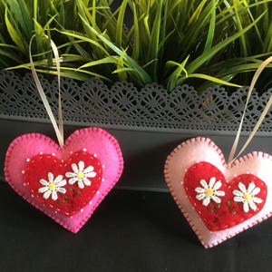 May include: Two felt heart ornaments with pink and red felt. Each heart has a white daisy embroidered on the red felt.