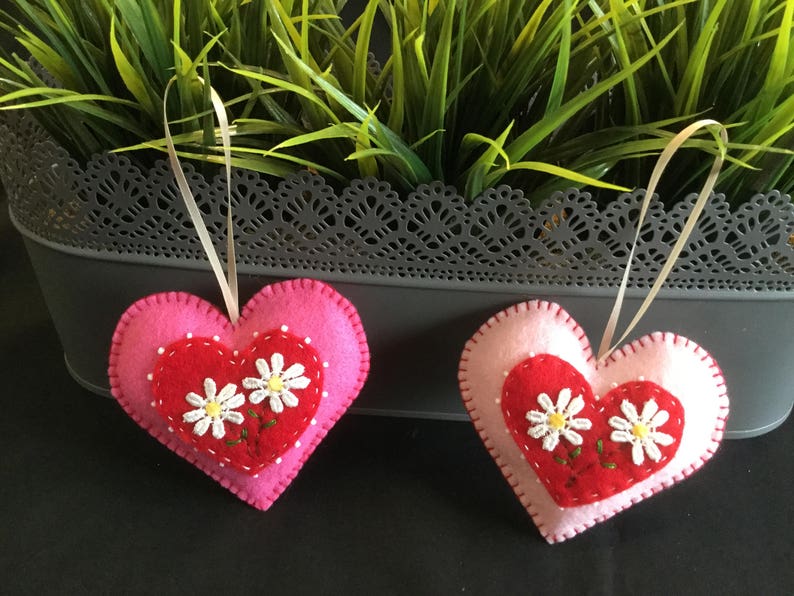 May include: Two felt heart ornaments with pink and red felt. Each heart has a white daisy embroidered on the red felt.