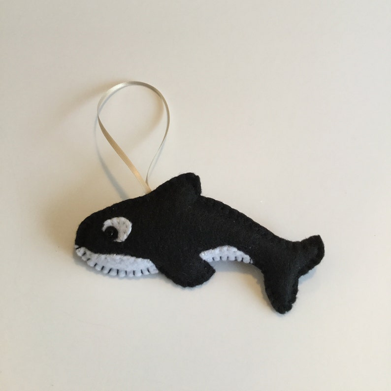 May include: A black and white felt ornament shaped like an orca whale with a white ribbon for hanging.