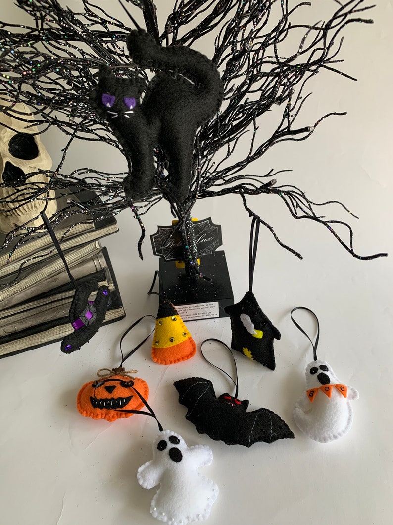 May include: A set of eight felt Halloween ornaments, including a black cat, a pumpkin, a ghost, a bat, a witch's hat, a candy corn, a ghost with "BOO" on it, and a black and yellow bat.