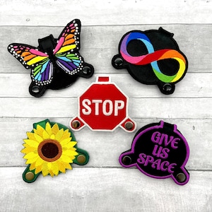 May include: Five colorful embroidered patches with velcro backing. The patches feature a butterfly, an infinity symbol, a stop sign, a sunflower, and a purple circle with the text "Give Us Space".