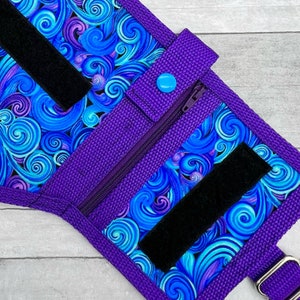 May include: Purple fabric pouch with a zipper closure, a blue button, and black velcro straps. The pouch has a swirling blue and purple pattern.