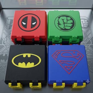 May include: Four square storage cases with hinged lids. The red case features a black Deadpool logo, the green case has a black Hulk fist icon, the black case displays a yellow Batman emblem, and the blue case shows a red Superman shield logo.