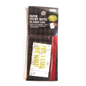 May include: Paper sticky notes in a slider case with a red zipper. The notes have a playing card theme with the text "Pick a card for today!" and various illustrations. The packaging is black and clear.