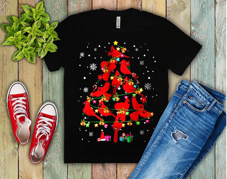 May include: Black t-shirt with a Christmas tree design featuring red cardinals, white snowflakes, and colorful lights.