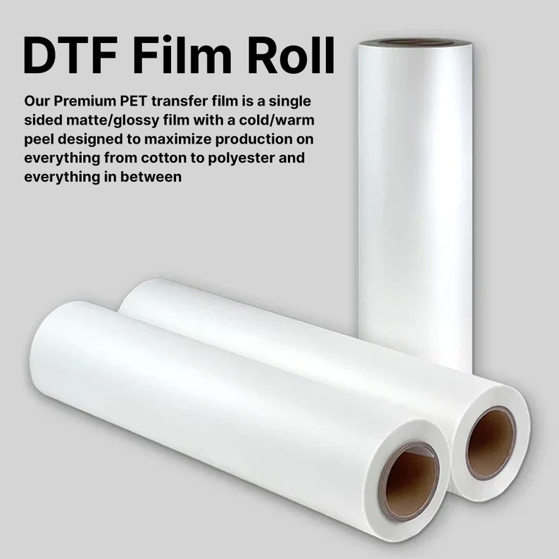 Pu&ograve; includere: Rotolo di pellicola DTF bianca. L'immagine mostra tre rotoli di pellicola DTF bianca, con il testo "DTF Film Roll" in alto. Il testo sottostante descrive la pellicola come una pellicola opaca/lucida a lato singolo progettata per massimizzare la produzione su vari materiali.