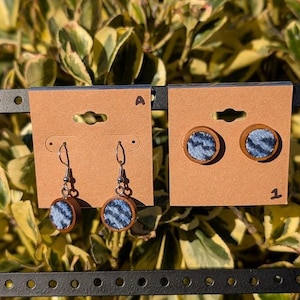 May include: A pair of blue and white patterned fabric earrings with wooden backing. The earrings are displayed on a brown card with the letter "A" and the number "1" printed on it.
