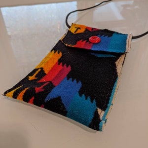 May include: A small black fabric pouch with a colorful geometric pattern. The pouch has a flap with a red button closure and a black cord for carrying.