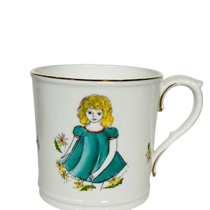 May include: White ceramic mug with a gold rim and a hand-painted illustration of a girl in a teal dress and yellow flowers.