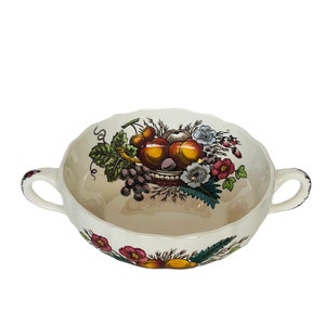 May include: A white ceramic soup bowl with two handles. The bowl features a colorful floral design with a basket of fruit, including apples, grapes, and cherries.