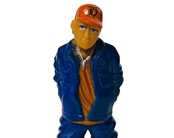 May include: A blue and orange figurine of a person wearing a blue jacket, orange shirt, and an orange baseball cap with a black letter "D" on it.