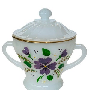 Peut inclure: Sucrier en céramique blanche avec couvercle, décoré de fleurs violettes et de feuilles vertes peintes à la main sur fond blanc. Le couvercle est orné d'une bordure dorée.