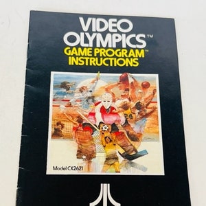 Puede incluir: Un manual de instrucciones en blanco y negro para el juego Atari Video Olympics. La portada presenta una ilustración colorida de atletas compitiendo en varios deportes, incluyendo baloncesto, natación y atletismo. El logotipo de Atari se muestra de forma prominente en la parte inferior del manual.
