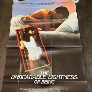 May include: A film poster for the movie "The Unbearable Lightness of Being", starring Daniel Day-Lewis, Juliette Binoche and Lena Olin. The poster features a black and white image of the actors in a bed, with the title of the film in large, white letters.