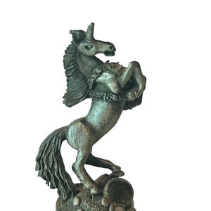 May include: A pewter figurine of a unicorn standing on a base with the letter "H" inscribed on it.