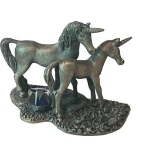 May include: A pewter figurine of a mother unicorn and her foal. The mother unicorn is standing with her head turned to look at her foal. The foal is standing with its head turned to look at its mother. The figurines are on a base with a small blue and green crystal.