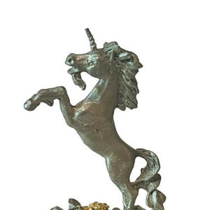 May include: A silver pewter figurine of a unicorn standing on its hind legs with its horn raised. The unicorn is standing on a rocky base with a gold and green jeweled crown.