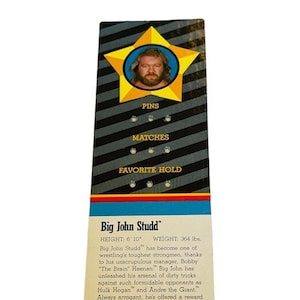 May include: A wrestling trading card featuring Big John Studd. The card is black and white with a yellow star in the top corner. The star has a picture of Big John Studd inside. The card has the text "Big John Studd", "Height: 6'10", "Weight: 364 lbs", "Pins", "Matches", "Favorite Hold", "Back Squeeze" and "C 1985 Titan Sports, Inc."