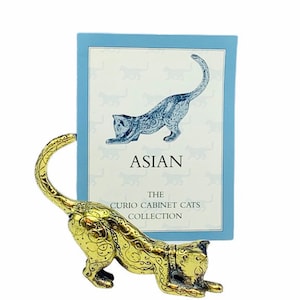 May include: A gold metal cat figurine with a curled tail, holding a card with the text "The Curio Cabinet Cats Collection" and "Asian" printed on it.