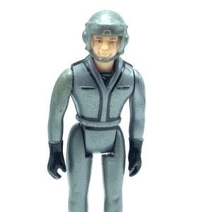 May include: A gray action figure wearing a silver helmet and a gray jumpsuit. The figure has a black face mask and black gloves.