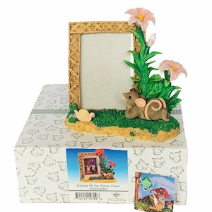 Könnte beinhalten: Eine kleine, braune Mausfigur mit einem roten Marienkäfer auf dem Kopf schaut hinter einem Weidenrahmen hervor. Der Rahmen ist von grünen Blättern und rosa Blüten umgeben. Der Text "Thinking of You Picture Frame" ist auf der Schachtel unter der Figur aufgedruckt.