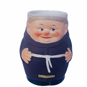 Puede incluir: Una taza de cerámica con forma de monje con un cinturón de cuerda blanco y la palabra "WIESBADEN" en la parte delantera.