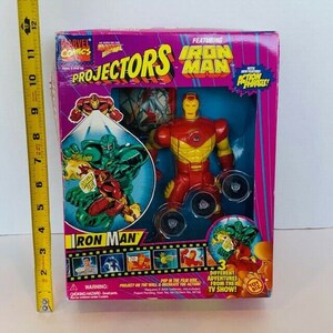 K&ouml;nnte beinhalten: Eine rote und gelbe Iron Man Actionfigur mit einer Projektionsscheibe. Die Verpackung zeigt das Marvel Comics Logo und die Worte "Projectors Iron Man". Die Figur h&auml;lt eine Scheibe, die verwendet werden kann, um Bilder an eine Wand zu projizieren. Die Verpackung enth&auml;lt auch ein Bild von Iron Man in Aktion.