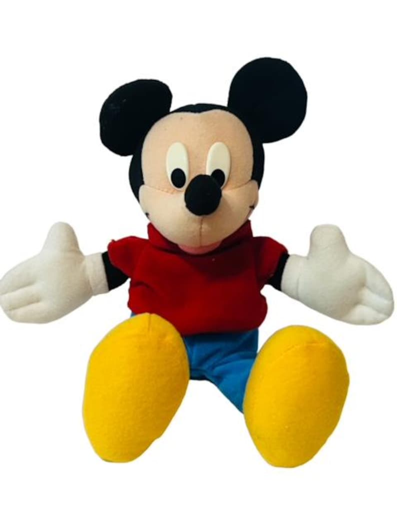 K&ouml;nnte beinhalten: Ein Pl&uuml;sch-Mickey-Mouse-Spielzeug, das ein rotes Hemd und eine blaue Hose tr&auml;gt. Das Spielzeug hat schwarze Ohren, eine schwarze Nase und wei&szlig;e Handschuhe.