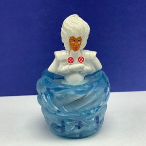 Peut inclure: Une figurine en plastique blanche de Storm des X-Men, avec une base tourbillonnante blanche et bleue. Elle porte un costume blanc avec des symboles rouges des X-Men sur la poitrine.