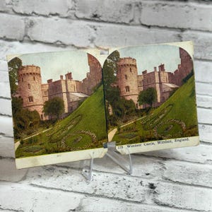 Puede incluir: Una tarjeta estereoscópica vintage que presenta una fotografía doble coloreada del Castillo de Windsor, en Inglaterra. La escena muestra torres de castillo de piedra, una colina cubierta de hierba y jardines. El texto 175 Windsor Castle, Windsor, England está impreso en la esquina inferior derecha.