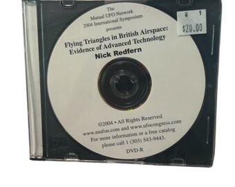 Puede incluir: Un disco DVD-R blanco con el texto "The Mutual UFO Network 2004 International Symposium presents Flying Triangles in British Airspace: Evidence of Advanced Technology Nick Redfern" y "©2004 All Rights Reserved www.mufon.com and www.ufocongress.com For more information or a free catalogue please call 1 (303) 543-9443. DVD-R". El disco está en una caja de plástico negro con una etiqueta de precio que dice "20,00 €".