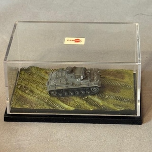 May include: A miniature gray tank model displayed in a clear plastic case. The tank sits on a green and brown terrain base. The case has a black base and a small "CAN-DO" sticker.
