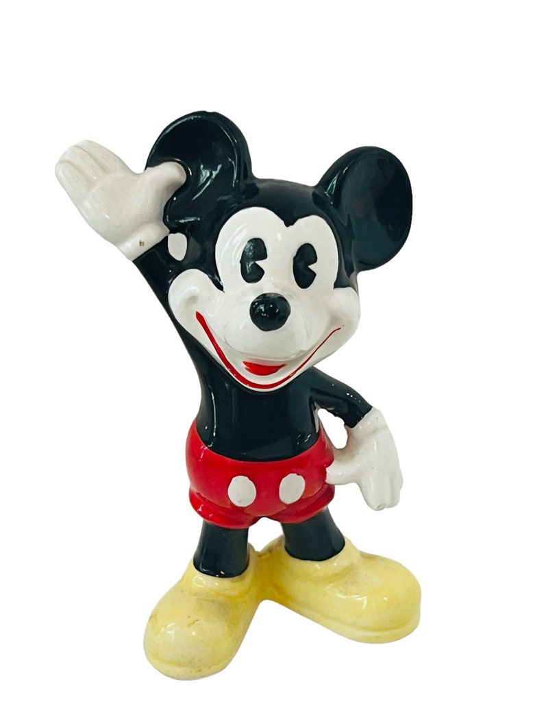 May include: A black and white ceramic figurine of Mickey Mouse. He is wearing red shorts with white buttons and yellow shoes. He is waving with his right hand.