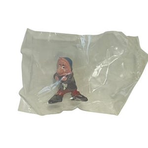 May include: A small plastic figurine of a cartoon character wearing a red and black outfit. The figurine is packaged in a clear plastic bag.