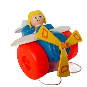 Könnte beinhalten: Ein vintage Spielzeugflugzeug zum Ziehen mit einem gelben Propeller und roten Rädern. Eine kleine blonde Figur sitzt im Cockpit.
