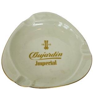 Op de afbeelding: Witte asbak van keramiek met een gouden rand en de woorden "Dujardin Imperial" en "1810" in gouden letters.