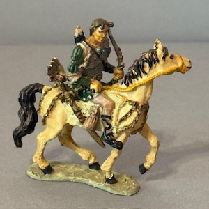 Puede incluir: Una figurita pintada de un guerrero montando un caballo blanco. El guerrero lleva ropa verde y marrón y sostiene un arco y una flecha. El caballo tiene una crin y una cola negras.