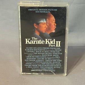 May include: A vintage cassette tape for "The Karate Kid Part II" soundtrack. The cover features images of the film's stars and the title in white lettering. The tracklist includes songs by Peter Cetera, The Moody Blues, and others.
