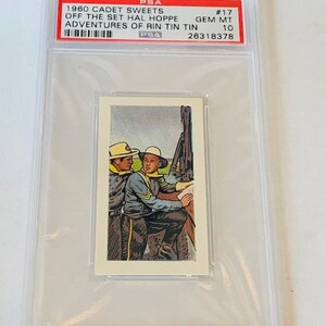 Pode incluir: Um cart&atilde;o classificado pela PSA que apresenta um cart&atilde;o de troca Cadet Sweets de 1960. O cart&atilde;o representa dois homens com uniforme, um segurando um mapa, com o texto "Off the Set Hal Hoppe Adventures of Rin Tin Tin #17 GEM MT 10 26318378" no r&oacute;tulo.
