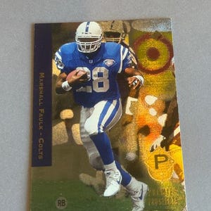 May include: A football trading card depicting Marshall Faulk of the Colts in a blue and white uniform, holding a football. The card has a gold foil background and the text "Premier Prospects".