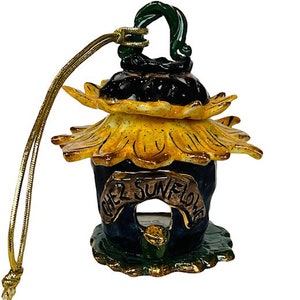 May include: A ceramic sunflower ornament with a gold cord. The ornament is painted in shades of yellow, green, and blue. The text "Chez Sunflower" is written on the front of the ornament.