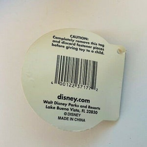 May include: White tag with black text and a barcode. The text reads "CAUTION: Completely remove this tag and discard fastener pieces before giving toy to a child."  The text also reads "disney.com Walt Disney Parks and Resorts Lake Buena Vista, FL 32830 &copy;DISNEY MADE IN CHINA"