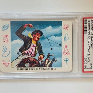 Puede incluir: Una tarjeta de colecci&oacute;n vintage con una ilustraci&oacute;n colorida de un gaucho argentino lanzando una bola. La tarjeta est&aacute; calificada PSA 9 y tiene el texto "1958 CARDO TRADING ARGENTINE GAUCHO THROWING BOLA - COW & INDI. #C-6 MINT 9 15522193 ARGENTINE GAUCHO THROWING BOLA" impreso en ella.