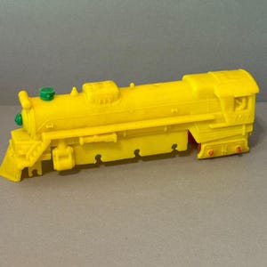 以下が含まれることがあります： 詳細なデザインの明るい黄色の玩具列車。列車は、フロントカウキャッチャー、緑色のトップの煙突、側面の番号707を備えています。ホイールには赤いアクセントが付いています。