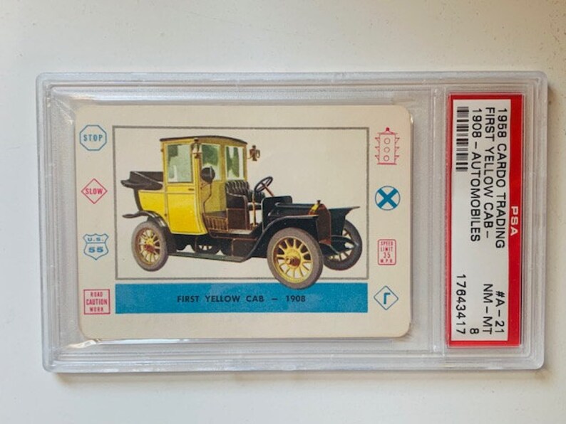 May include: A vintage 1958 Car-Do Trading card featuring a yellow 1908 First Yellow Cab automobile. The card is graded NM-MT 8 by PSA and has the number #A-21.