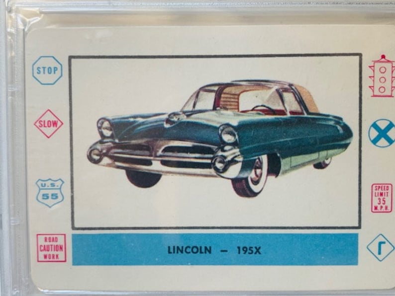 Puede incluir: Un coche Lincoln 195X azul turquesa con detalles cromados. El coche est&aacute; sobre un fondo blanco con varias se&ntilde;ales de tr&aacute;fico, incluyendo una se&ntilde;al de stop, una se&ntilde;al de reducci&oacute;n de velocidad, una se&ntilde;al de l&iacute;mite de velocidad y una se&ntilde;al de obras en la carretera.